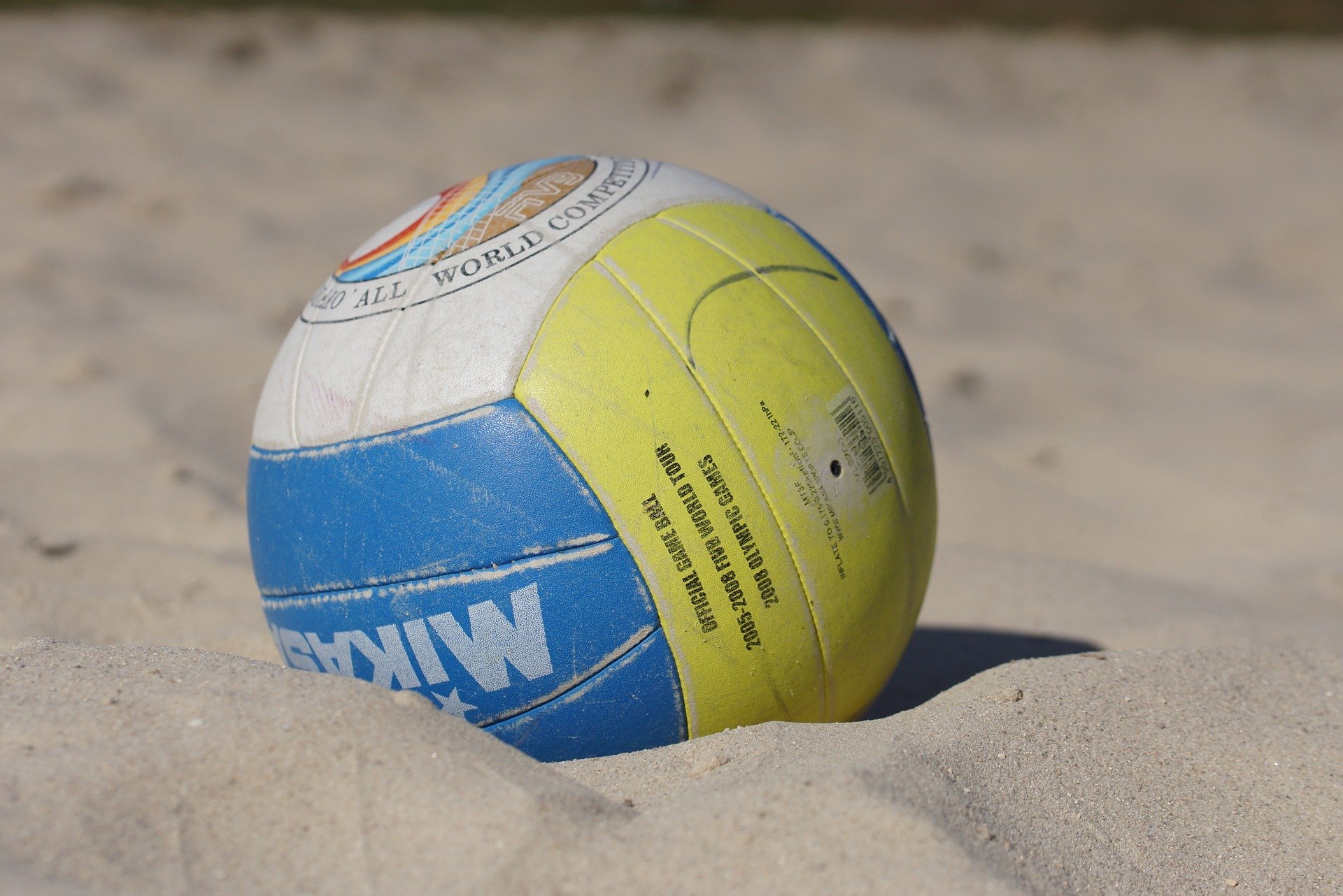 A blue, white, and yellow volleyball lies partially buried in the sand